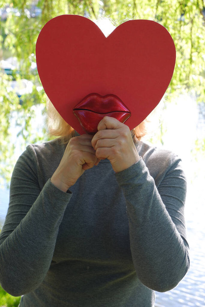The girl sends an air kiss with large red decorative lips with a paper heart. World Kiss Day. - Photo, Image