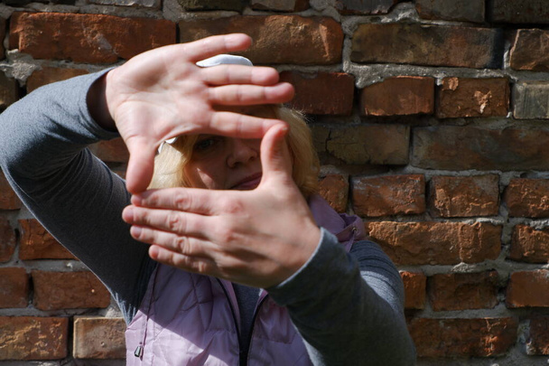 Una chica cerca de una pared de ladrillo con las manos imagina una cámara. Día de San Veronicas Día de los Fotógrafos . - Foto, Imagen