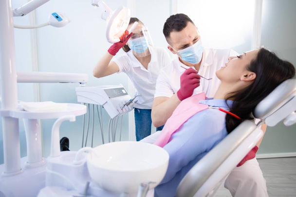 Dwóch dentystów leczy zęby młodej pacjentki. Kobieta siedząca na krześle dentystycznym. Opieka zdrowotna, medycyna - Zdjęcie, obraz