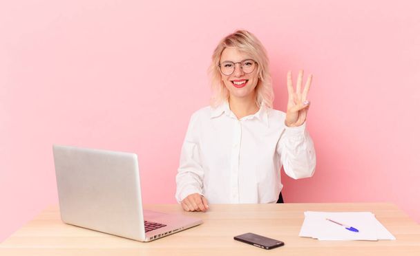 blonde pretty woman young pretty woman smiling and looking friendly, showing number three. workspace desk concept - Foto, Imagen