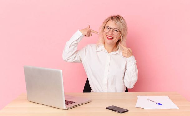 blonde pretty woman young pretty woman smiling confidently pointing to own broad smile. workspace desk concept - Foto, Imagem