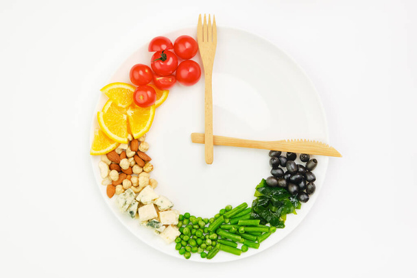 Comida colorida e talheres arranjados na forma de um relógio em uma chapa. Jejum intermitente, dieta, perda de peso, conceito de hora de almoço. - Foto, Imagem