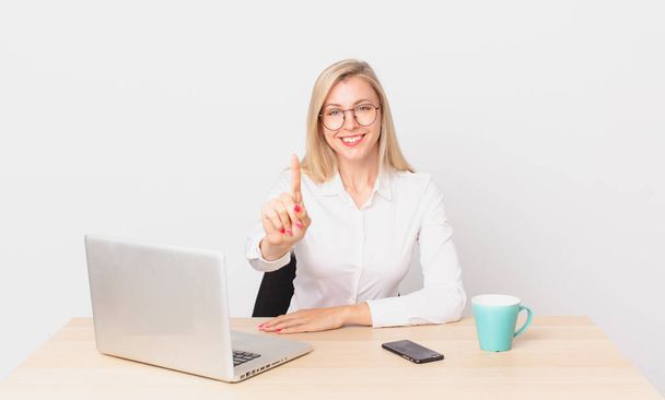blonde pretty woman young blonde woman smiling proudly and confidently making number one and working with a laptop - 写真・画像