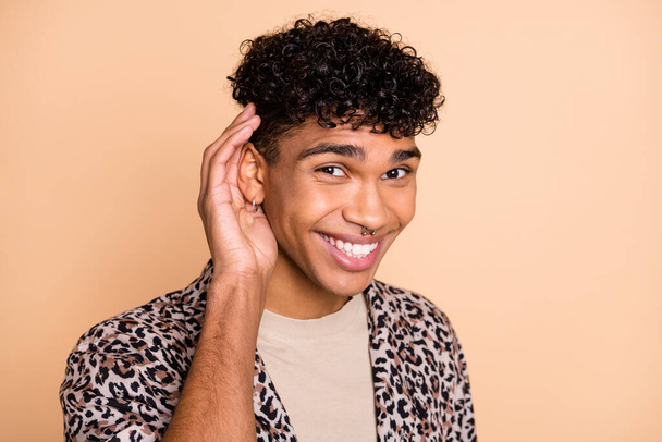 Portrait of brunet optimistic guy hand ear wear modern shirt isolated on pastel beige color background - 写真・画像