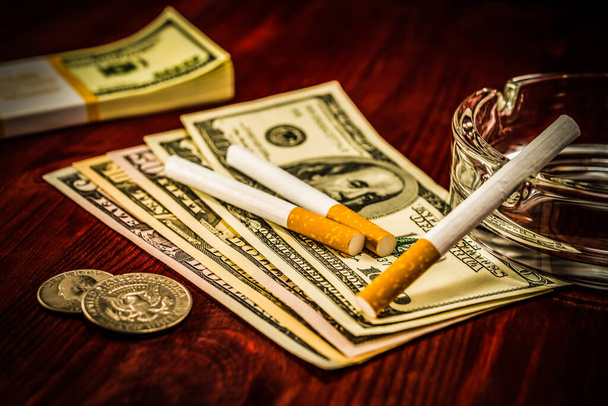Two cigarettes are on the dollars, lies next to a pack of bills  - Foto, Imagem