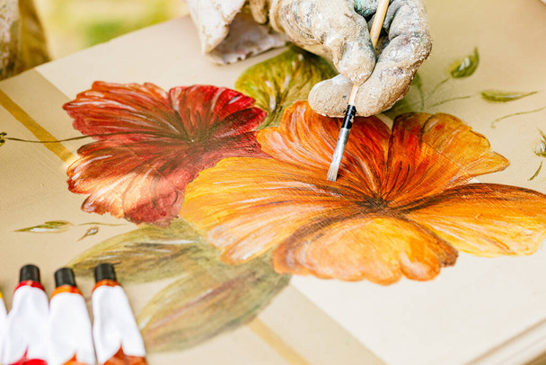Nierozpoznawalna osoba malująca kwiaty na drewnianej powierzchni. remonty mebli i stolarstwa. rękawiczki do rysowania ze szczotkami. - Zdjęcie, obraz