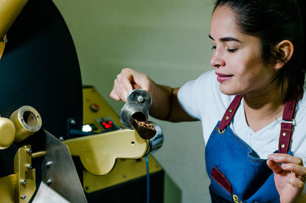 Une femme mains rôtir les grains de café aromatiques de café sur une machine moderne utilisée pour rôtir les grains. - Photo, image