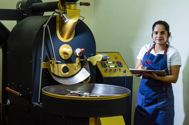 Een vrouw handen roosteren de aromatische koffiebonen van koffie op een moderne machine gebruikt om bonen te roosteren. - Foto, afbeelding