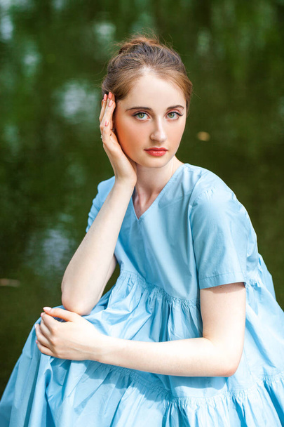Portrait of a young beautiful woman in a lush turquoise dress posing against the background of a pond in a summer park - Фото, зображення