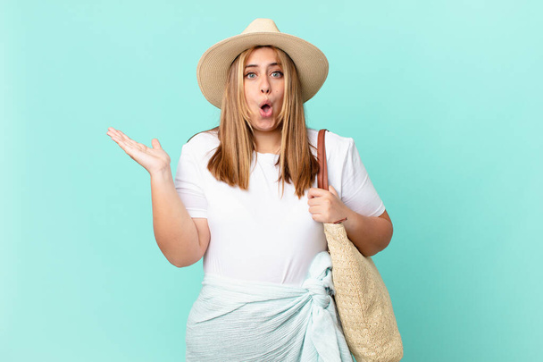 curvy pretty blonde woman looking surprised and shocked, with jaw dropped holding an object - Фото, изображение