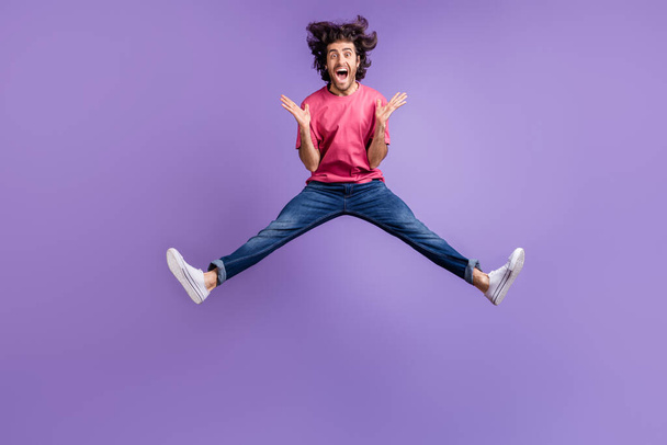 Full size photo of impressed nice brunet guy jump wear pink t-shirt jeans isolated on violet background - Zdjęcie, obraz