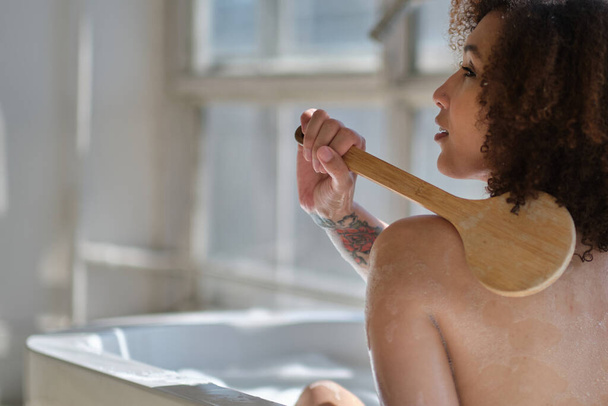 Gülümseyen ve rahatlatan Afro-Amerikan kadın köpük dolu bir küvette banyo yapıyor. Harika bir zaman. Yaşam tarzı insan kavramı - Fotoğraf, Görsel