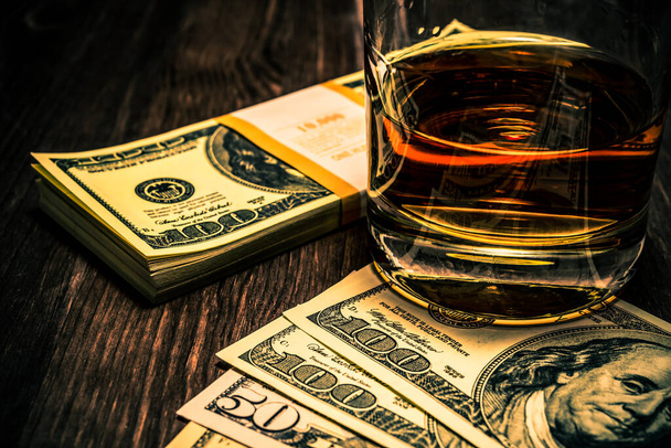 Glass of whiskey with pack of dollars on a wooden table. Close u - Fotó, kép