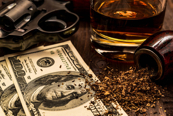 Glass of whiskey and revolver with a money and tobacco pipe on t - Foto, Bild