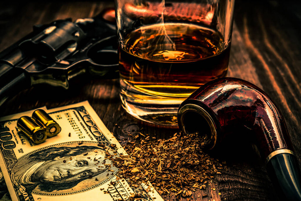 Glass of whiskey and revolver with a money and tobacco pipe on t - Фото, зображення