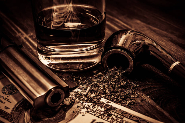 Üzerinde para ve tütün piposu olan bir bardak viski ve tabanca. - Fotoğraf, Görsel