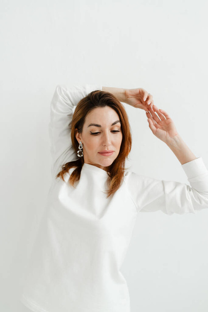 beautiful girl with red hair in a white sweater holds her hands above her head - Foto, Imagen