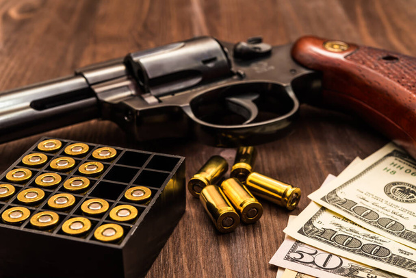 Revolver with cartridges and money on the wooden table - Foto, Bild