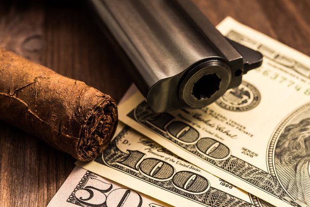 Barrel of a revolver with cuban cigar and money on the wooden ta - Fotoğraf, Görsel
