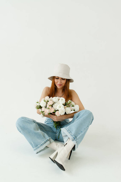 piękna dziewczyna z bukietem kwiatów w kapeluszu panama i niebieskie dżinsy na tle cykloramy - Zdjęcie, obraz