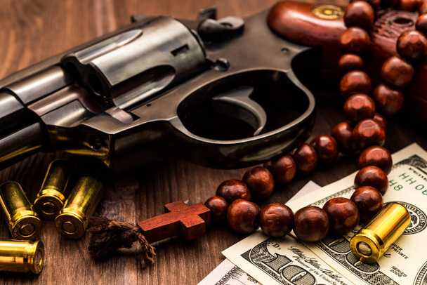 Revolver with cartridges and a rosary on the wooden table. Close - Foto, imagen