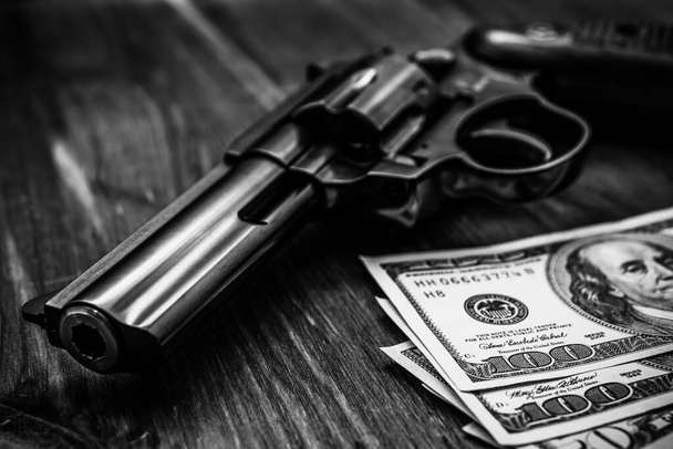 Revolver and money on the wooden table. Close up view, focus on  - Photo, image
