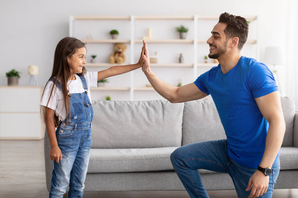 Vader en dochter geven high five in de woonkamer - Foto, afbeelding