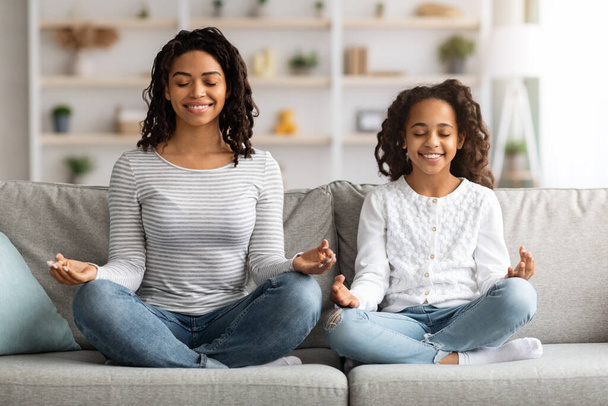 Entspannte schwarze Mutter und Tochter sitzen auf der Couch und meditieren - Foto, Bild