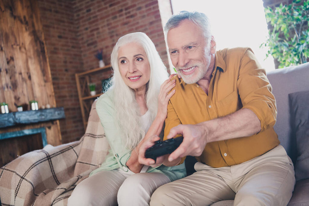 Photo of happy nice charming grey haired couple sit sofa smile play game support indoors inside house flat - Fotó, kép