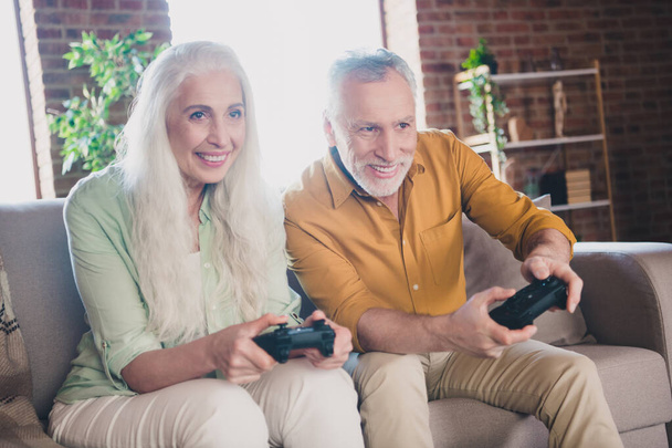 Photo of pretty funky pensioner lady gentleman sitting couch enjoying playstation smiling indoors house flat - Foto, Bild