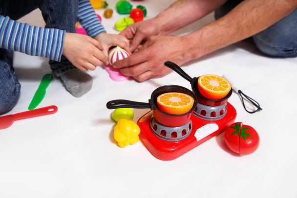 Dad and daughter play with sliced plastic vegetables and fruits with Velcro, cooks food on a toy stove in a bowl. Children's cooking, a girl learns to cook. White background, close-up. Father's Day - Fotoğraf, Görsel