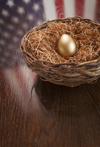 zlaté vejce v hnízdě s americkou vlajkou reflexe na stole - Fotografie, Obrázek