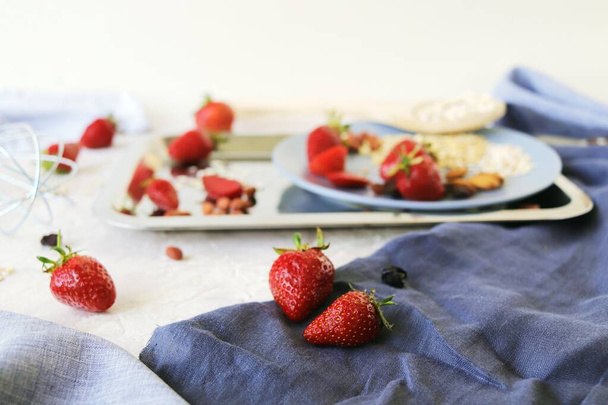 Healthy breakfast ingredients on the table, strawberries, oatmeal and nuts on a light background - Photo, Image