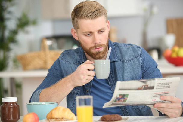 handsome young man having breakfast and reading newspaper at home - 写真・画像