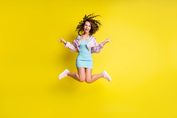 Full size photo of happy funky funny crazy girl jumping showing tongue rocknroll sign isolated on yellow color background - Foto, Imagem