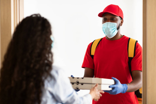 Czarny dostawca w masce medycznej trzymający pudełka po pizzy - Zdjęcie, obraz