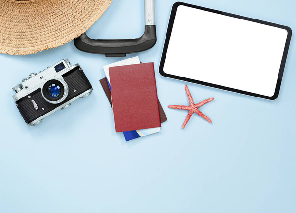 чемодан, солнечная шляпа, планшетный компьютер, фотоаппарат, морская звезда, паспорт и билеты на светло-голубом фоне - Фото, изображение