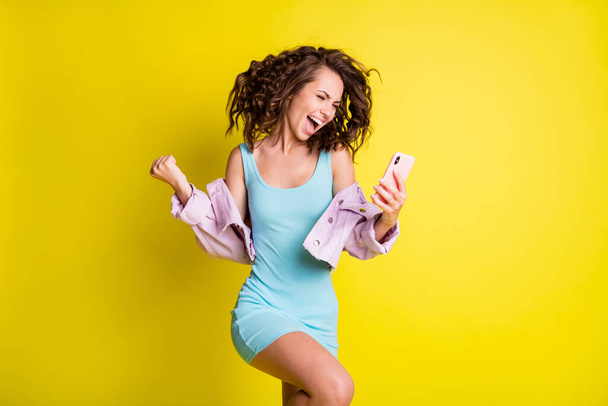 Fotografie šťastné vzrušený šílený usmívající se dívka zvednout pěsti ve vítězství úspěch vyhrát loterii v telefonu izolované na žlutém pozadí barvy - Fotografie, Obrázek