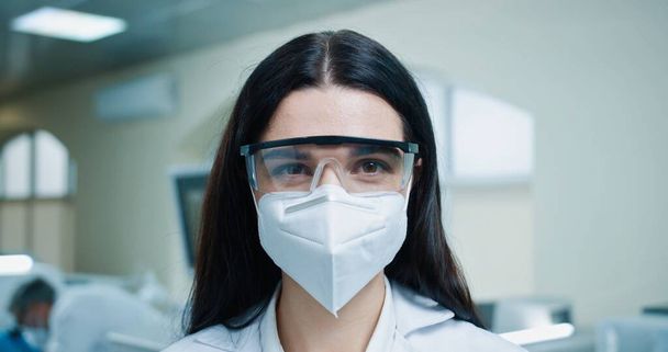 Close up portrait of happy young beautiful Caucasian female medical specialist wearing protective mask and goggles and looking at camera. Healthcare worker, lab scientist, laboratory work - Foto, immagini