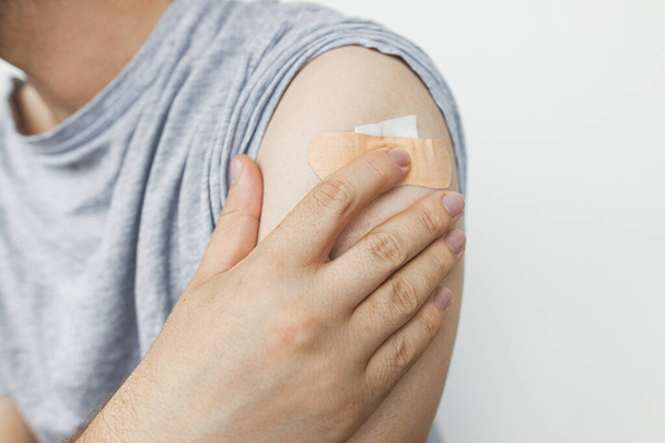 Клейкая повязка на руке человека после инъекции вакцины Ковид-19 на белом фоне, крупным планом. Кампания коронавирусной вакцинации. Профилактика, лечение и защита от Covid-19 - Фото, изображение