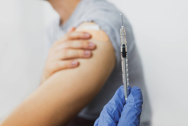 Concept de vaccination contre le coronavirus. Seringue avec le vaccin Covid-19 dans la main du médecin sur le fond de l'homme tenant le bras avec un bandage adhésif après injection. Programme d'immunisation Covid-19. - Photo, image