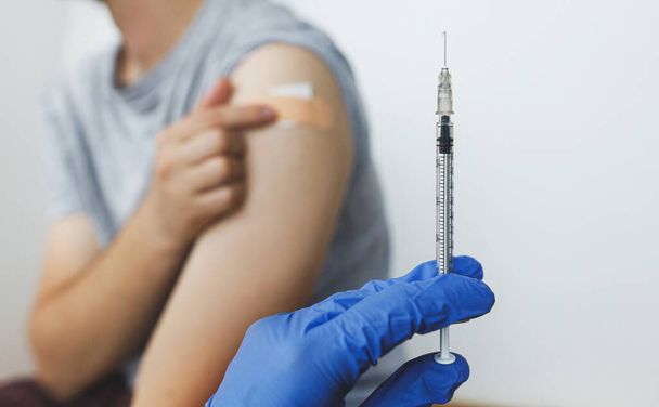 Coronavirus-Impfkonzept. Spritze mit Covid-19 Impfstoff in der Hand des Arztes auf dem Hintergrund des Mannes, der den Arm nach der Injektion mit einem Klebeverband hält. Covid-19-Impfprogramm. Virenschutz - Foto, Bild