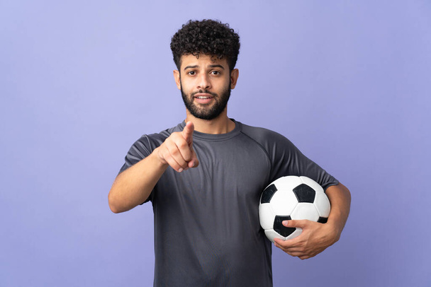 Bonito marroquino jovem jogador de futebol homem sobre isolado no fundo roxo surpreso e apontando frente - Foto, Imagem