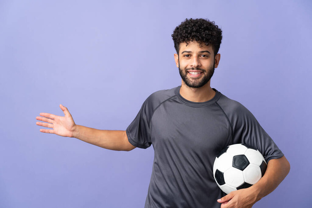 ハンサムなモロッコの若いサッカー選手男上の分離された上に紫色の背景に手を伸ばし側に招待するために来る - 写真・画像