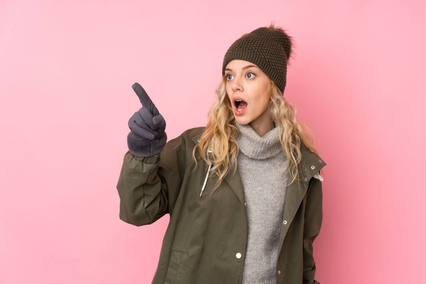 Young girl with winter hat isolated on pink background pointing away - Φωτογραφία, εικόνα