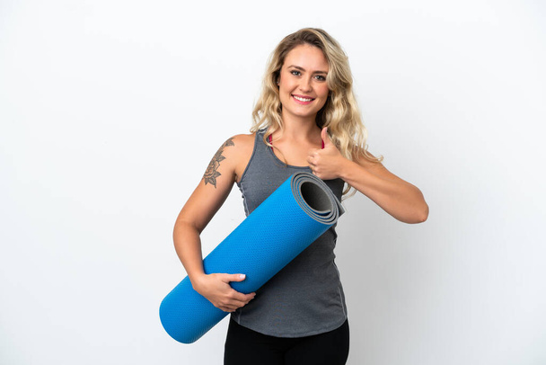 Young sport Brazilian woman going to yoga classes while holding a mat isolated on white background with thumbs up because something good has happened - 写真・画像