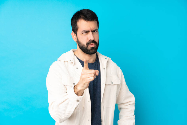 Young handsome man with white corduroy jacket over isolated blue background frustrated and pointing to the front - Photo, Image