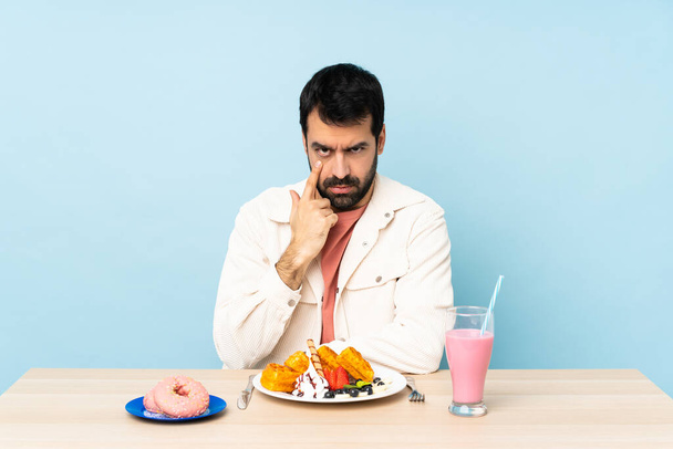 Человек за столом, завтракающий вафлями и молочный коктейль, показывающий что-то - Фото, изображение