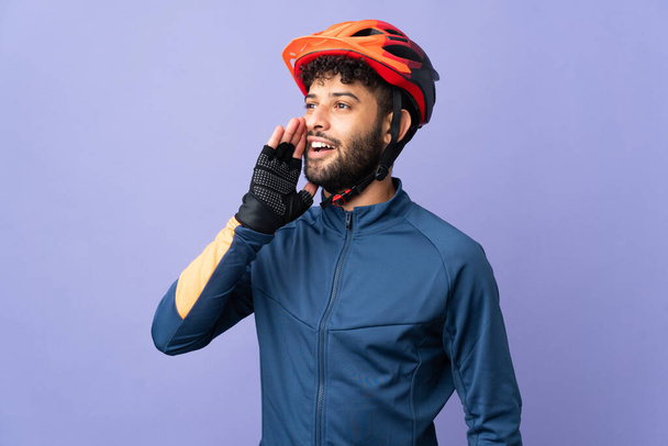 Young Moroccan cyclist man isolated on purple background shouting with mouth wide open to the side - Fotoğraf, Görsel