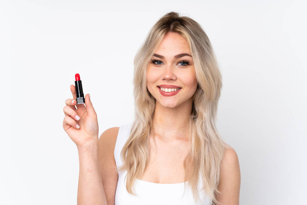 Teenager blonde girl over isolated white background holding red lipstick - Foto, Imagem